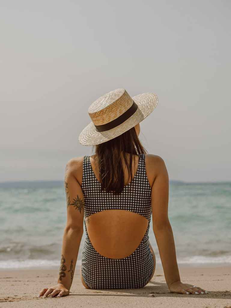 woman with tattoos in swimsuit and hat resting on sandy beach